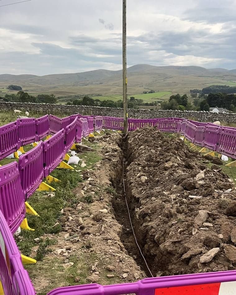 Open trench across fell land with barriers either side and hills behind