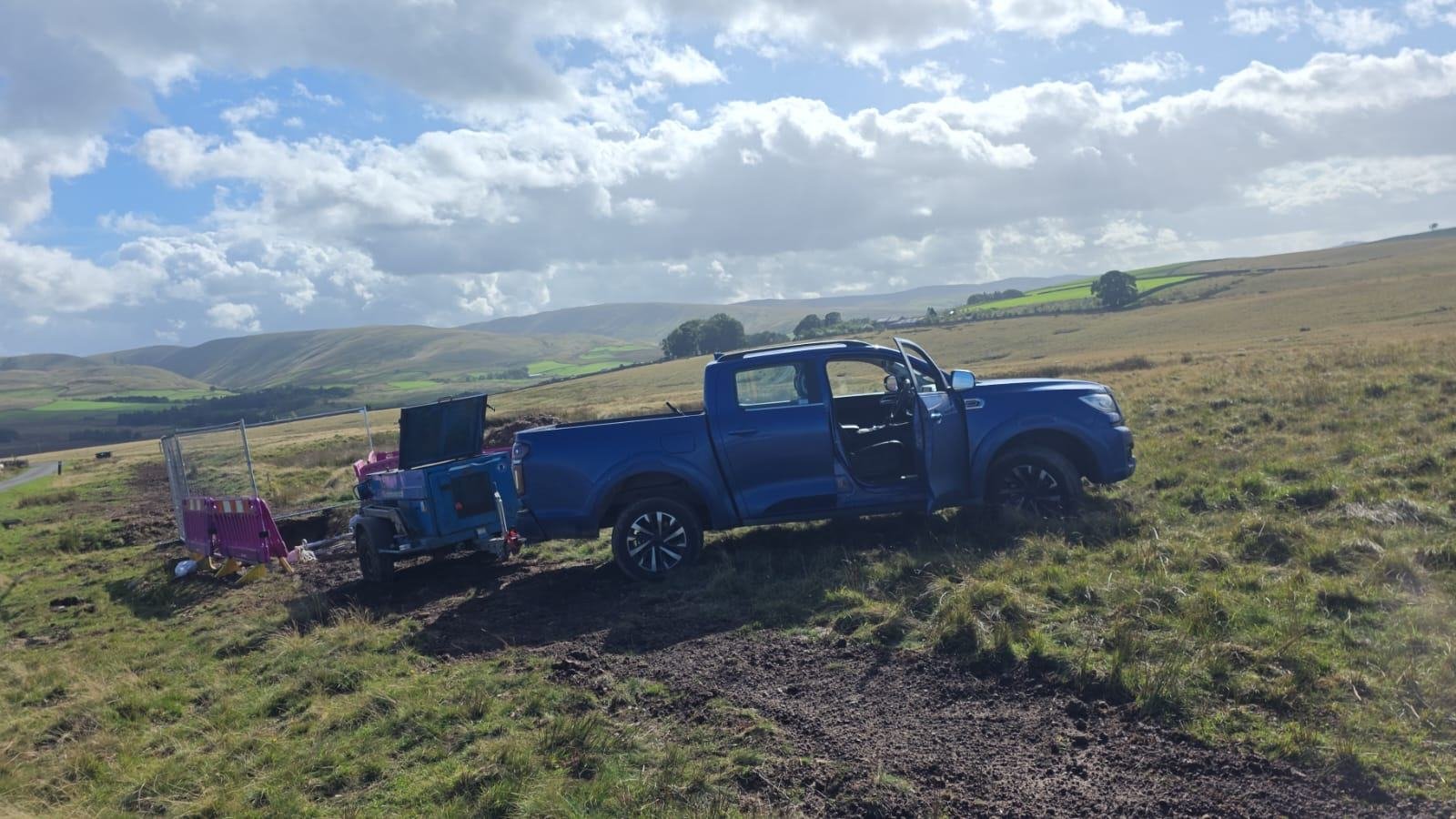 Pickup and welfare trailer parked on open fell beside a fenced excavation