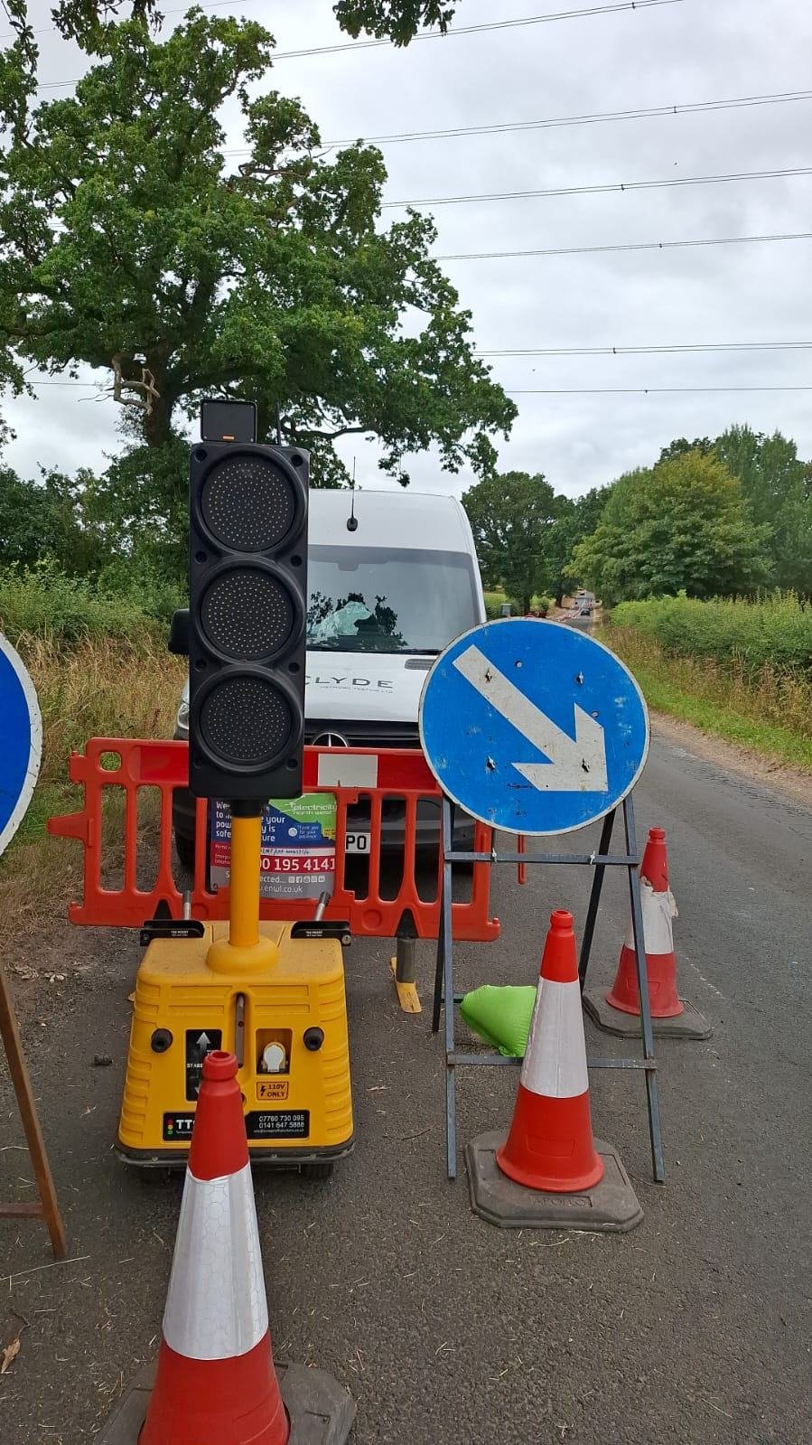 Portable traffic light and keep-left sign in front of a Clyde van on a rural road