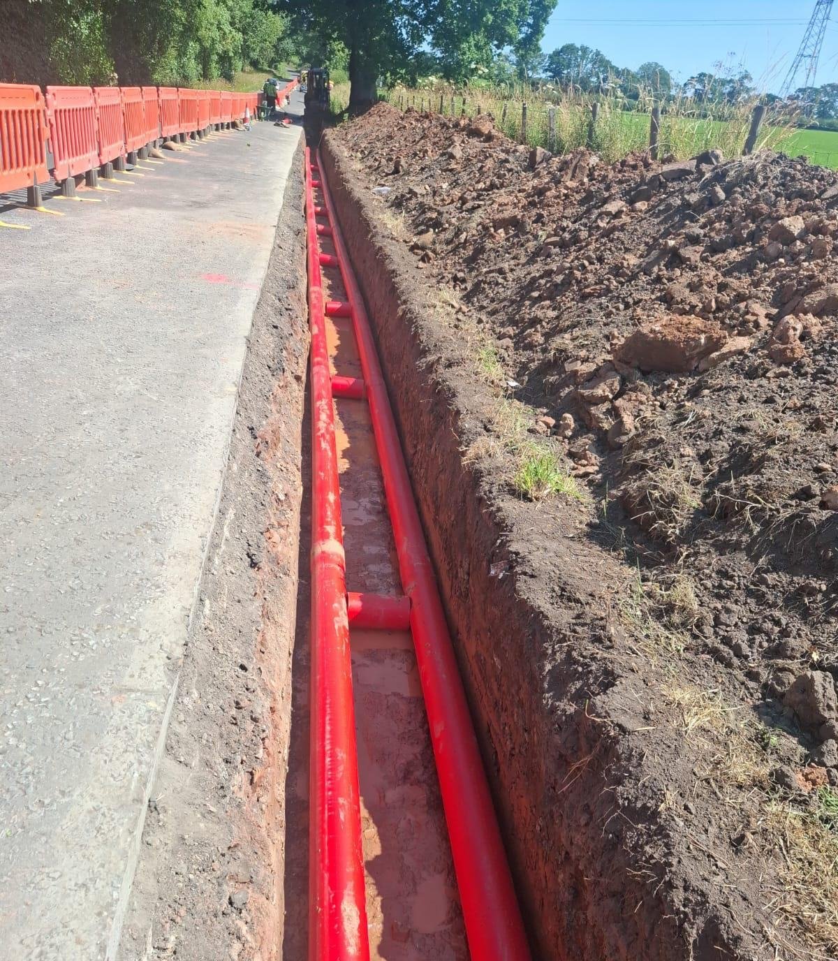 Open HV duct trench along a rural road with barriers in place