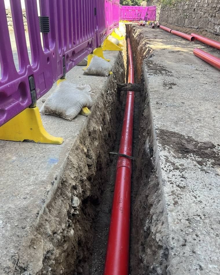 Red duct laid in a footway trench passing beneath existing services