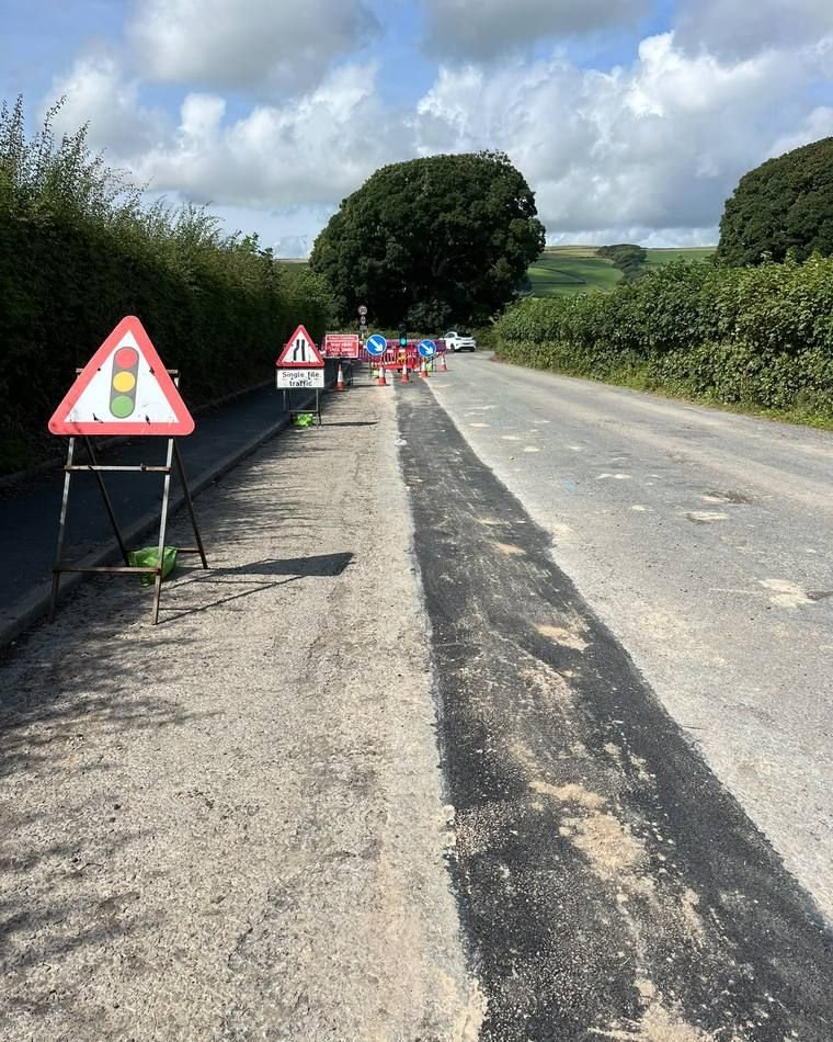 Rural carriageway with fresh permanent tarmac reinstatement along the route